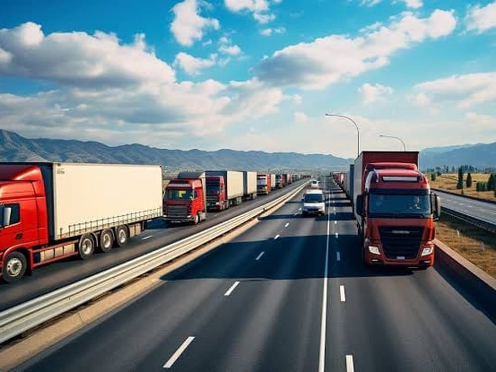 Line of cargo trucks on a multi-lane highway with mountains in the distance
