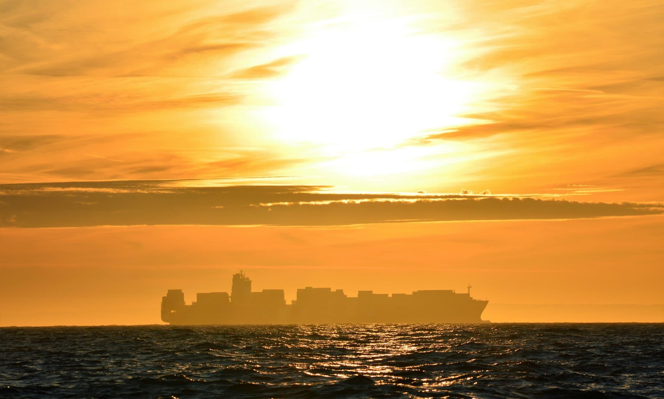 Cargo ship silhouetted against the sea at sunset